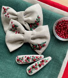 two bow ties with red berries and green leaves on them sitting next to a bowl of cranberries