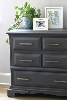 a black dresser with two pictures on top and a potted plant next to it