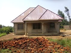 a small house with a metal roof in the middle of a dirt field next to grass and trees