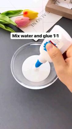 a person pours water into a glass bowl with tulips in the background