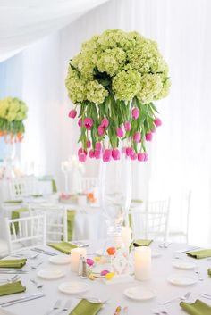 a vase filled with pink and green flowers on top of a table next to candles