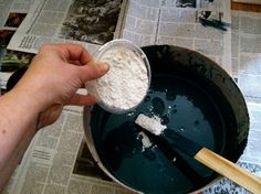 a person scooping flour into a pan on top of a newspaper with a wooden spoon