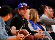 a man in a detroit blue hat smiles as he sits next to other people at a basketball game