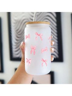 a person holding up a white mason jar with pink bows painted on it and a straw in the lid