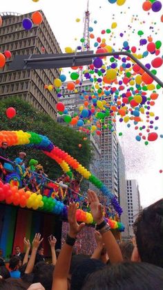 many balloons are being flown in the air above a city street as people look on