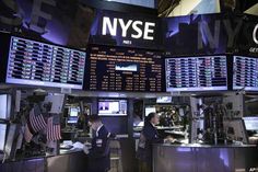 people are standing in front of the new york stock exchange at night, with many screens showing financial information