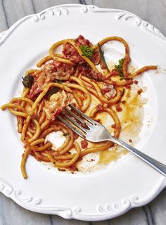 a white plate topped with spaghetti and meat next to a fork on top of a table