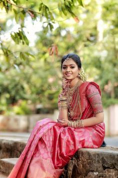 a woman in a red and gold sari sitting on some steps with trees behind her