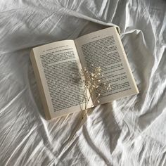 an open book sitting on top of a bed covered in white sheets next to a plant