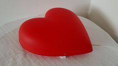 a red heart shaped lamp sitting on top of a white tablecloth covered bedding