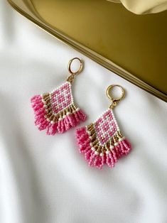 pink and gold beaded earrings on white cloth next to metal box with golden handle