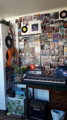 a room with a keyboard, guitar and many pictures on the wall behind it in front of a plant