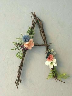 a letter made out of branches and flowers on top of a white wall with the words custom