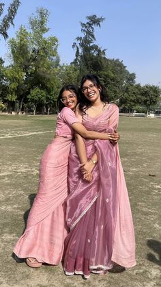 two women standing next to each other in a field smiling for the camera with their arms around one another