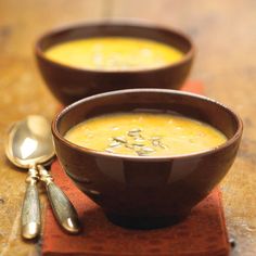 two brown bowls filled with soup on top of a wooden table next to spoons