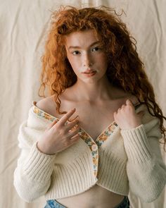 a woman with red hair wearing a white sweater and blue jean shorts is posing for the camera