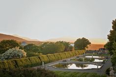 the sun is setting over an ornamental garden with water and hedges in front of it