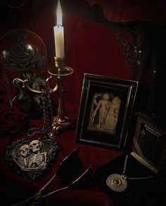 a table topped with pictures and a lit candle next to a framed skeleton on a red cloth