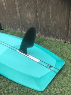 a blue surfboard sitting in the grass next to a wooden fence with a paddle on it