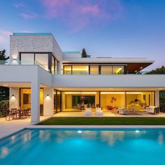 a modern house with an outdoor pool in the foreground and patio furniture on the other side