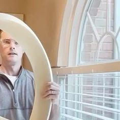 a man holding up a large white object in front of a window