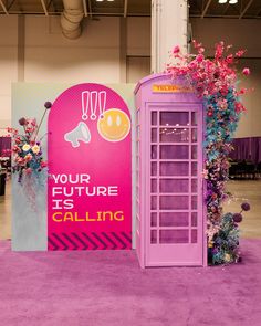 a purple phone booth with an advertisement on the wall and flowers in front of it