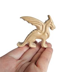 a hand holding a small wooden toy with a dragon on it's back and wings