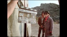 two men standing next to each other in front of a sign