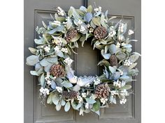 a wreath on the front door with pine cones and greenery hanging from it's sides