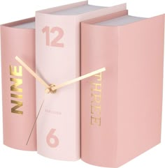 a clock made out of pink books with gold numbers on the face and hands, sitting next to each other