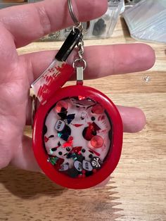 a hand holding a red keychain with lots of small objects in it on top of a wooden table