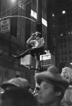 a man sitting on top of a street light in the middle of a crowded city