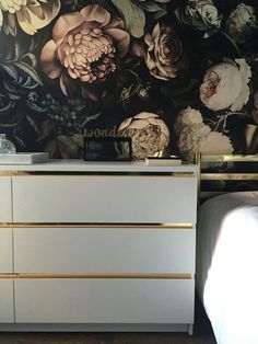 a white dresser sitting next to a wall with flowers on it