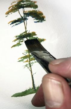 a person holding a paintbrush in front of a drawing of a pine tree on a white wall