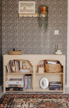 a book shelf with books and magazines on it in front of a wallpapered wall