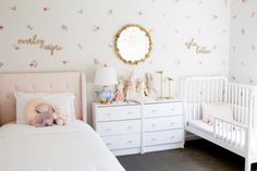 a baby's room with two white cribs and pink flowers on the wall