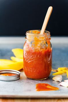 a jar filled with red sauce sitting on top of a table next to yellow flowers