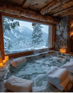 an indoor hot tub with candles in front of a large window overlooking the snow covered mountains