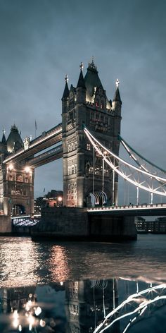 the tower bridge is lit up at night with lights reflecting in the water below it