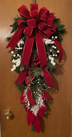 a christmas wreath hanging on a door with red bows and white flowers in the center