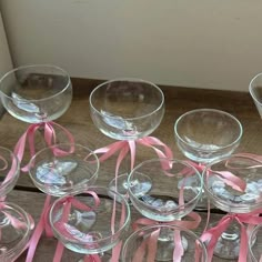 there are many wine glasses with pink ribbons around them on the wooden table and one is empty