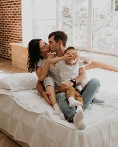 a man and woman sitting on top of a bed with a baby in their lap