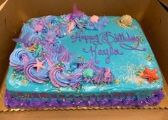 a birthday cake in a box with purple and blue frosting, stars and seashells