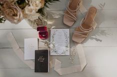 a table topped with flowers and shoes next to a wedding card, candle and ring