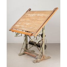 an old drafting table with a wooden top and metal frame on the bottom, in front of a white wall