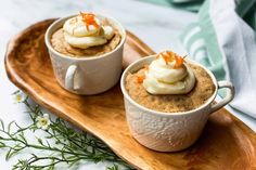 two cups filled with dessert sitting on top of a wooden tray