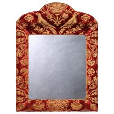 a red and gold mirror with an ornate design on the bottom, in front of a white background