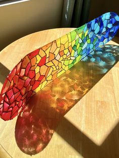 a stained glass vase sitting on top of a wooden table next to a window with the sun shining through it