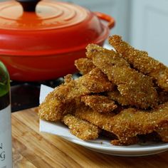 some fried food on a white plate next to a bottle of wine and a red pot