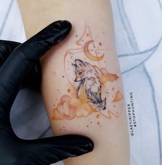 a woman's arm with a watercolor tattoo of a fox and moon on it